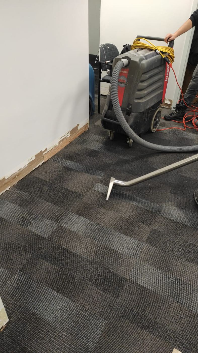 Portable extractor removing water from commercial carpet tile with baseboards removed for drying